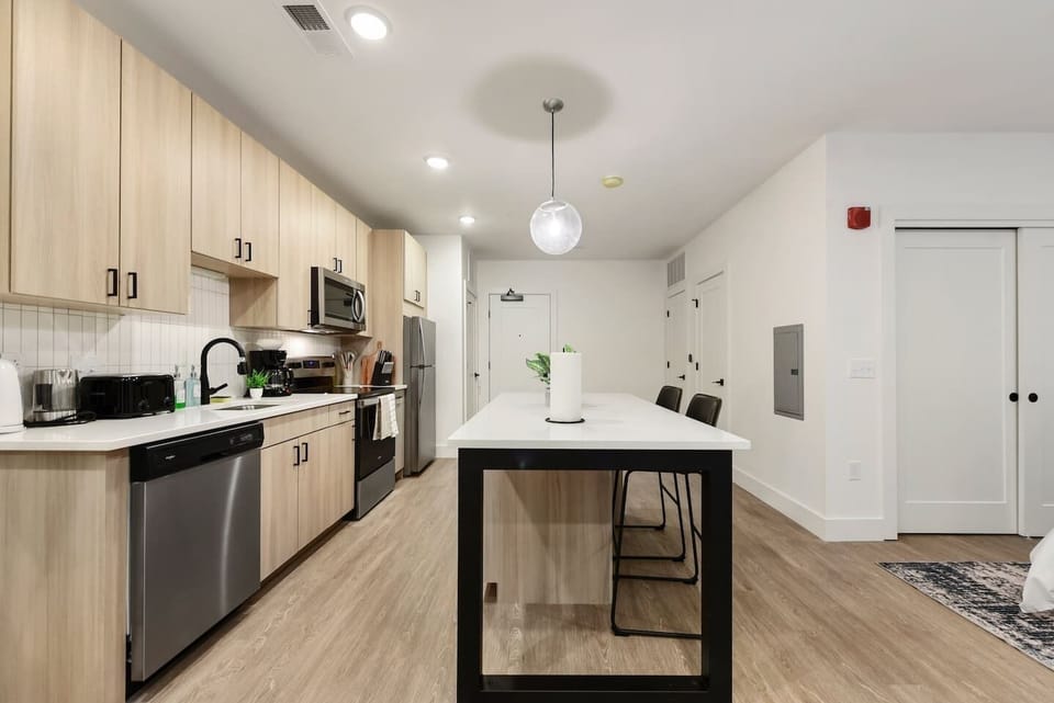 Modern kitchen with sleek appliances and island seating—fully stocked with a rice cooker, coffee machine, kettle, pots, pans, and more.