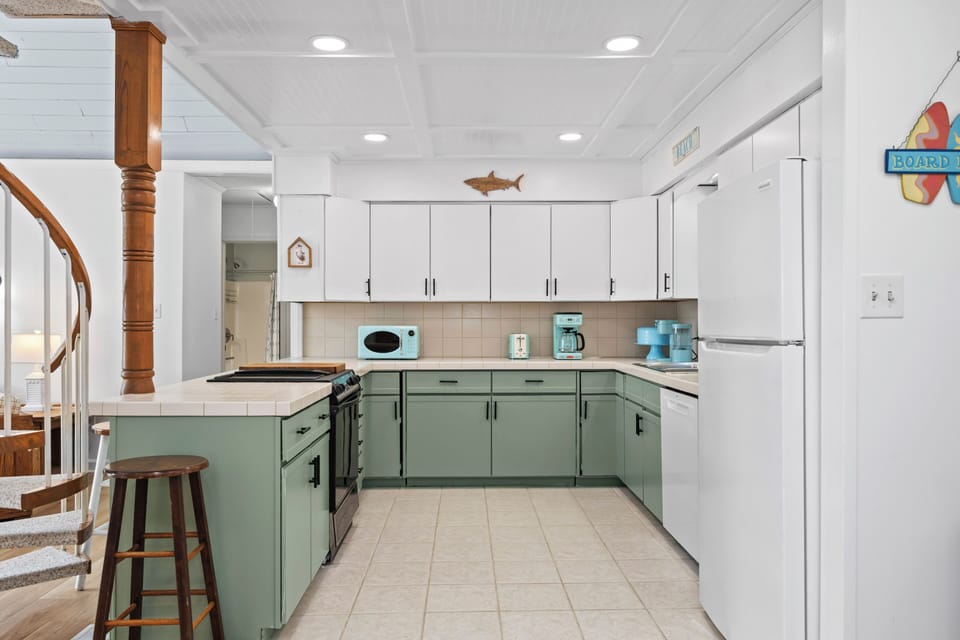Your fully equipped kitchen features coastal charm with sage-green cabinetry, ample counter space, and everything you need to prepare meals during your stay.