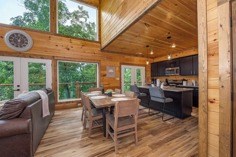 Step into your sunlit retreat where soaring cathedral ceilings and panoramic forest views create the perfect backdrop for relaxing meals and cozy evenings in your private woodland escape.