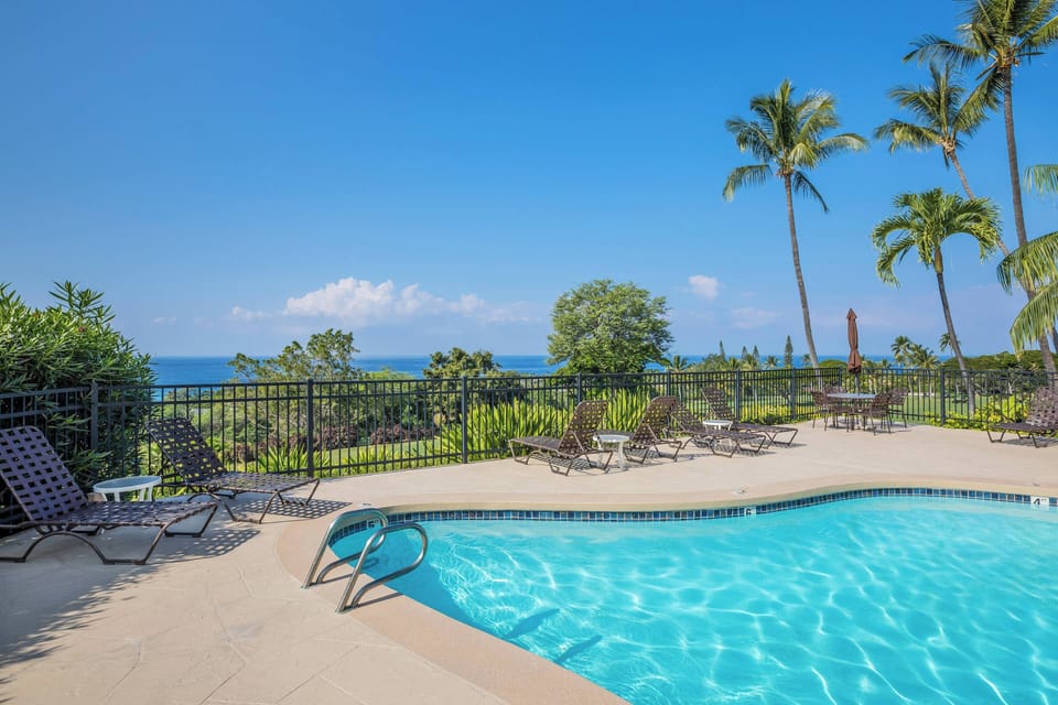 A sparkling pool deck overlooking lush tropical gardens and brilliant ocean views, framed by swaying palms and loungers ready for your island escape.