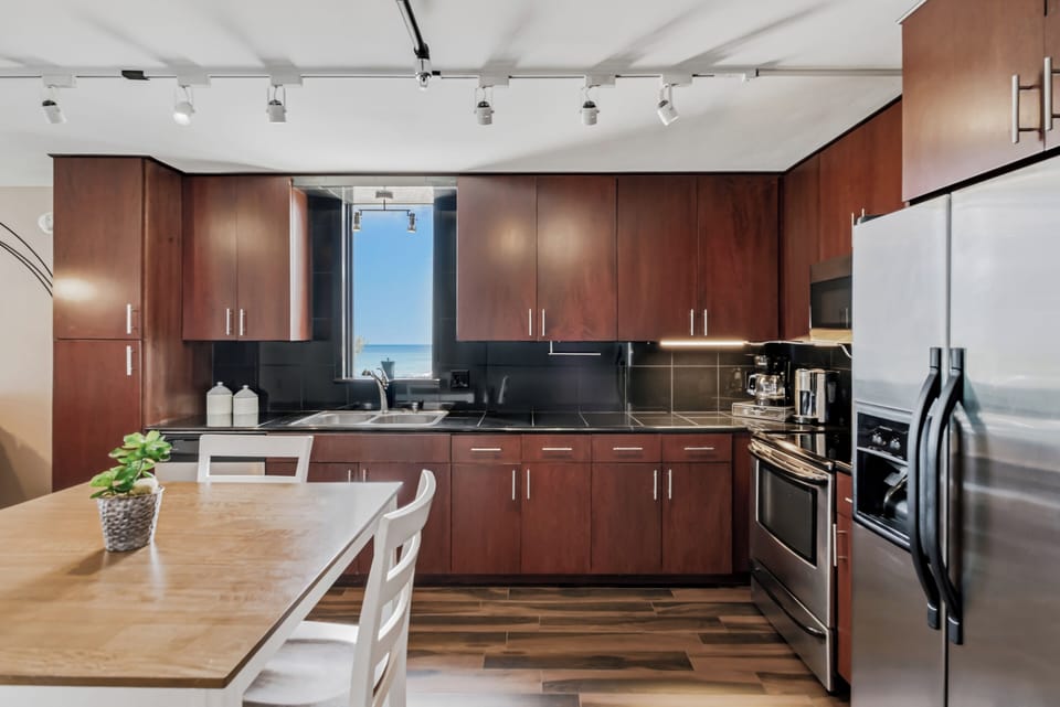 Cook with a view—your modern, fully equipped kitchen features sleek cabinetry, stainless steel appliances, and an inspiring ocean view through the window above the sink.