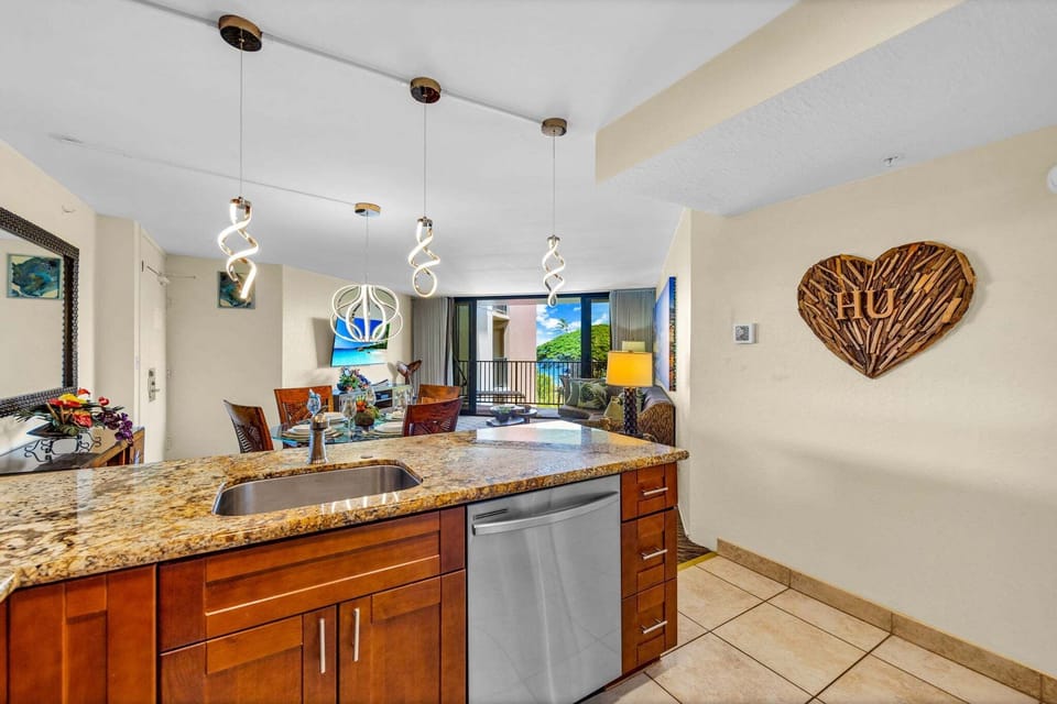 Open layout where granite counters meet tropical accents, flowing into a sunlit living space.