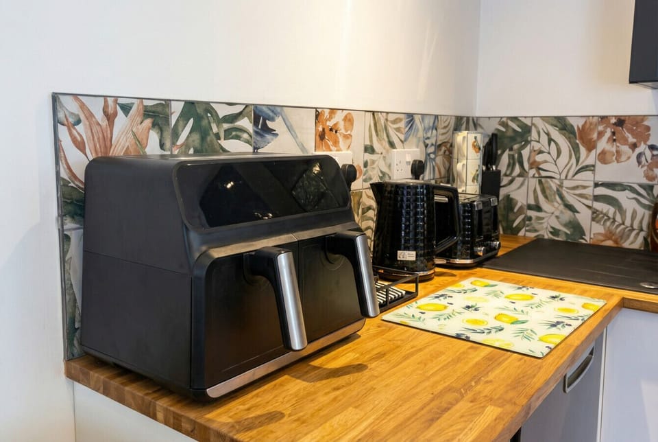 A dual-basket air fryer, toaster, kettle, and botanical splashback tiles make this kitchen as stylish as it is practical.