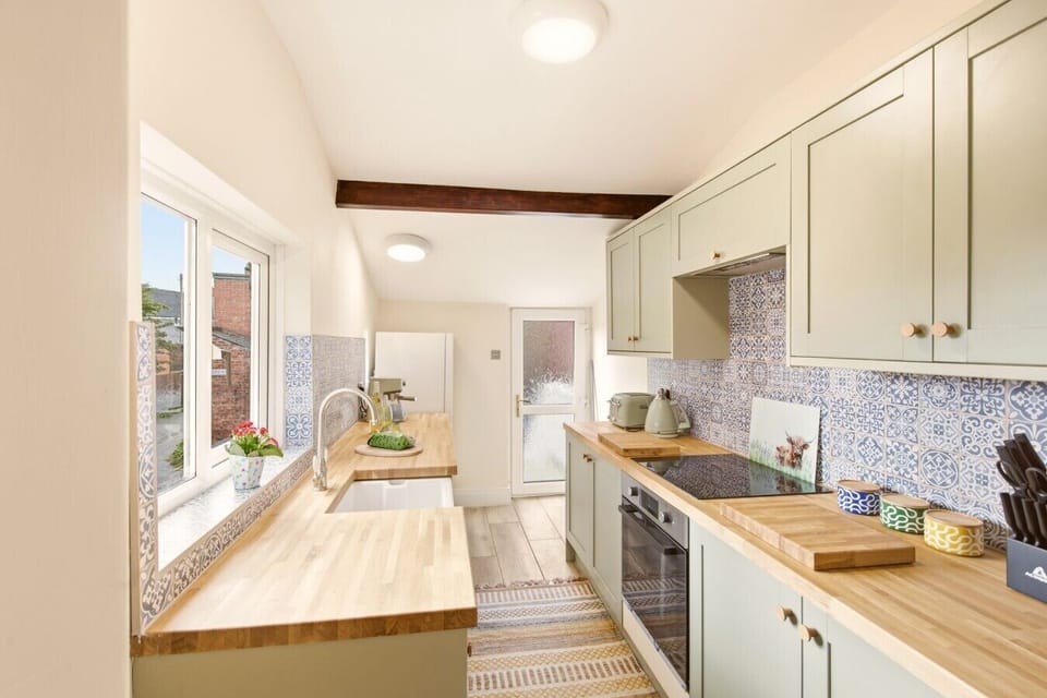 Galley kitchen with wooden worktops and blue patterned splashback.