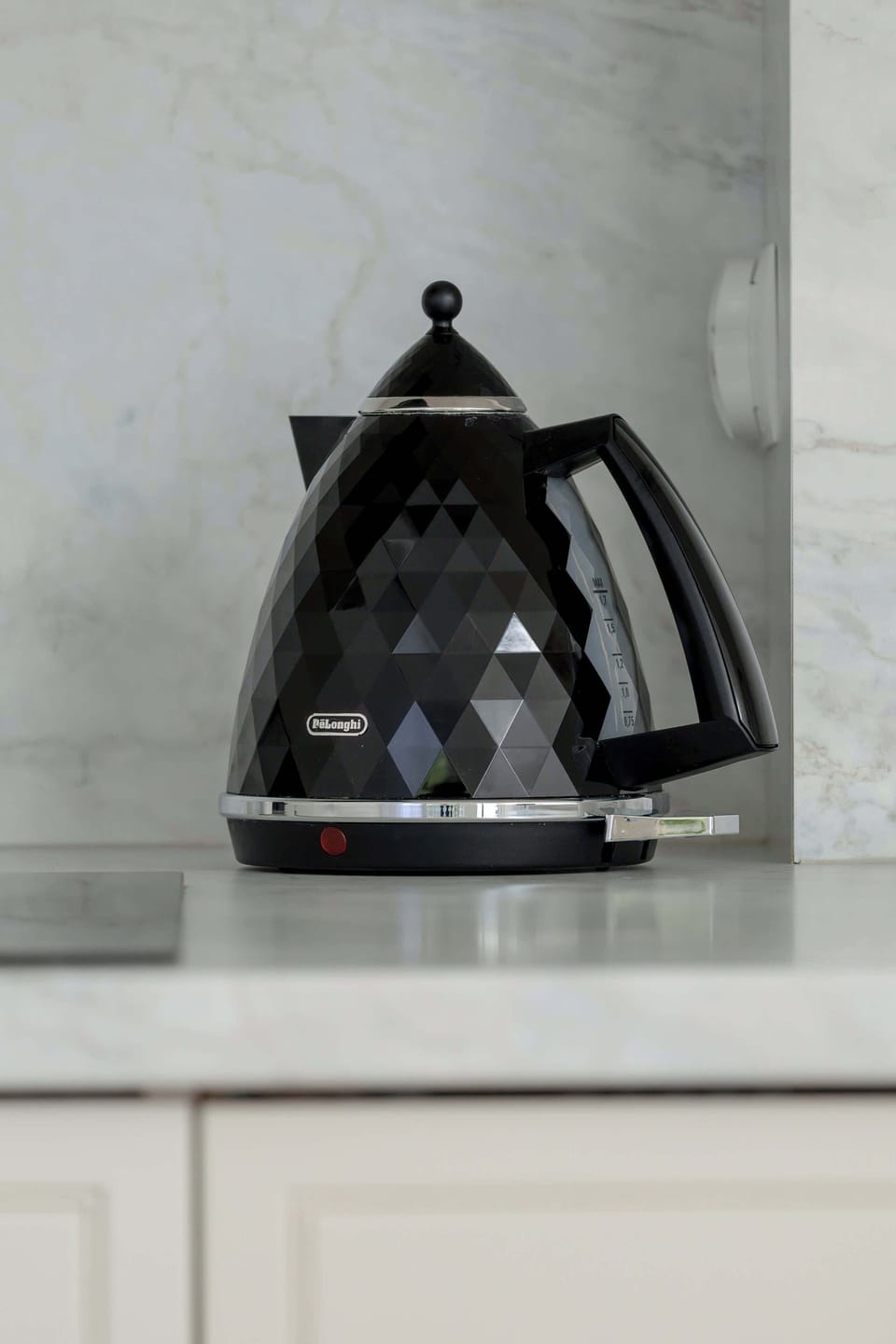A focused detail shot of a black electric kettle sitting on a polished kitchen counter. The minimalist backdrop emphasizes a clean and modern design.