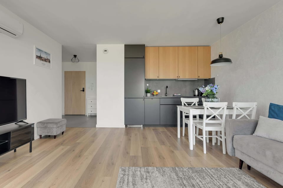 Apartament oferuje jasny salon z rozkładaną sofą, telewizorem, klimatyzacją oraz częścią jadalnianą. Duże przeszklenia prowadzą na przestronny balkon z meblami wypoczynkowymi i widokiem na okolicę.