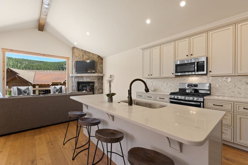 Gather around the spacious island where bright mountain views frame your culinary adventures. The sleek kitchen seamlessly blends modern amenities with warm stonework and natural wood accents.