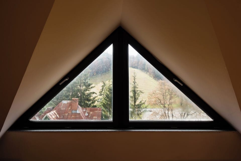 Triangular attic window with panoramic views over Predeal's pine forest and surrounding mountains. A signature architectural detail that fills the living area with natural light and mountain atmosphere.
