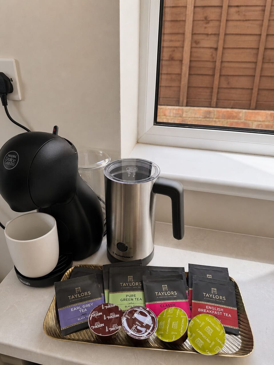 A breakfast bar station featuring a coffee machine, milk frother, and complimentary teas and coffees.