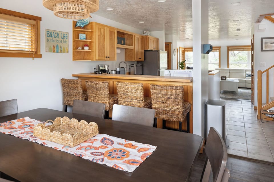 Dining room with a spacious table and hutch stocked with wine and cocktail glasses, plus a home bartending set--everything you need to mix up your favorite cocktail and unwind after a day at the beach.