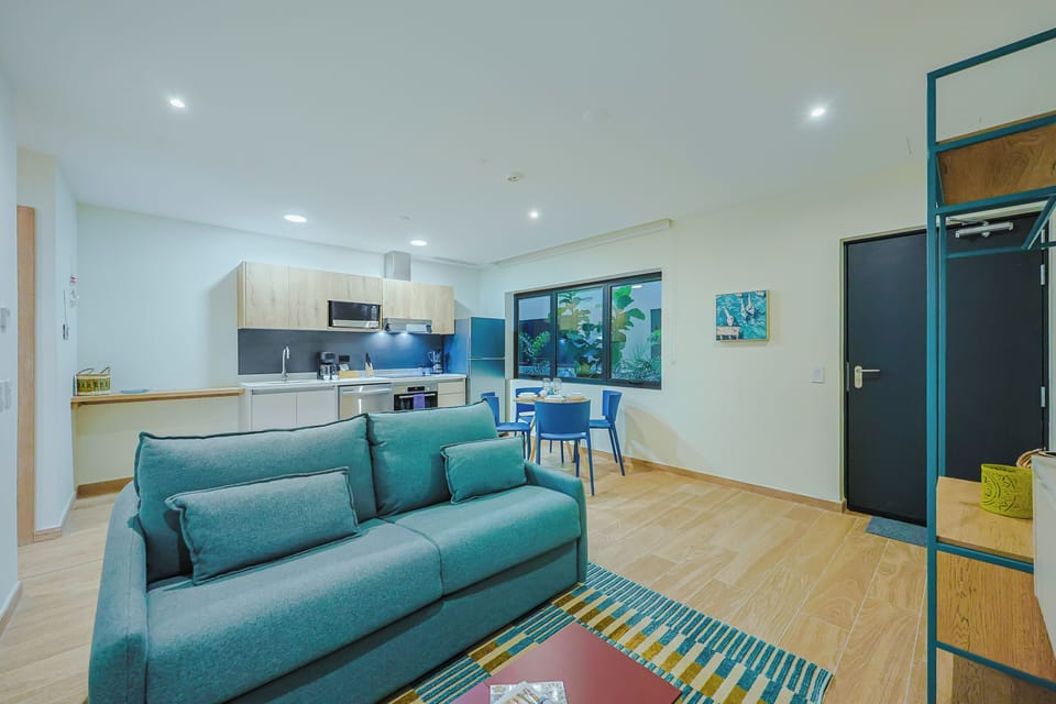 Step into your open-plan retreat where modern living flows effortlessly. Settle into the cozy teal sofa, enjoy meals at your dining table, or whip up fresh snacks in your fully equipped kitchen—everything you need for a relaxing stay.