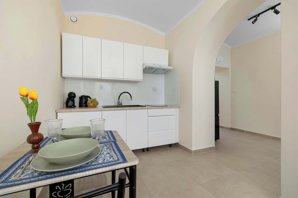 A compact white kitchen with upper cabinets, a refrigerator, and a dining table positioned nearby.