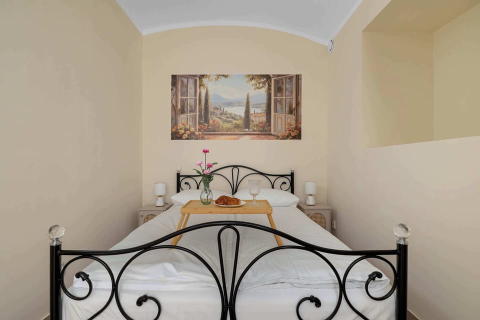 Another view of the bedroom, featuring the ornate metal bed frame, white bedding, bedside tables, and decorative artwork above the bed.