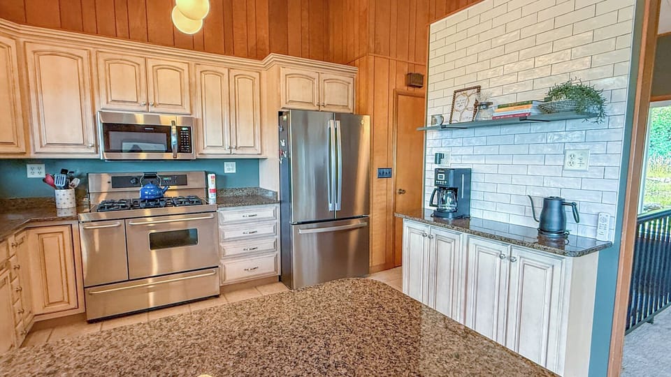 Your fully equipped kitchen features granite countertops, stainless steel appliances, and a charming mix of wood paneling and white subway tile, creating a warm and inviting space for preparing meals during your stay.