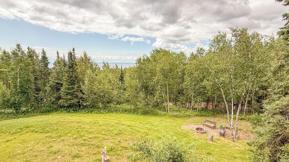 The property sits on a tranquil hillside surrounded by lush forest and expansive open lawn, offering a peaceful natural setting with distant mountain views.