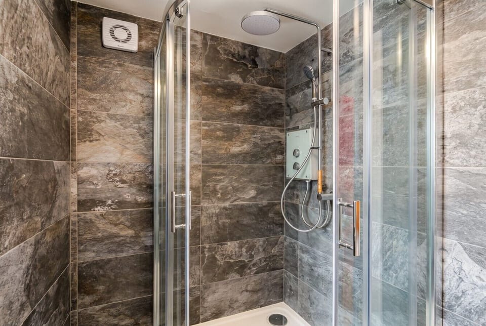 Sleek stone-tiled walk-in shower with rainfall head.