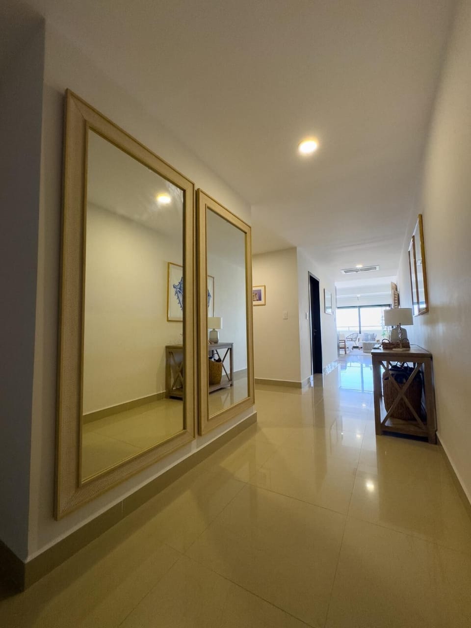 Hallway features large beige-framed mirrors, glossy tile floor, wooden console table with lamp, and framed artwork.