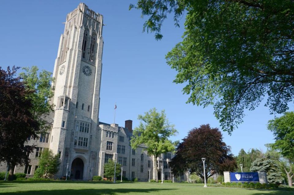 Historic stone building with a clock tower and manicured grounds near Toledo