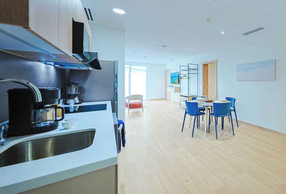 Your bright, open-plan living space features a fully equipped kitchen, stylish dining area with vibrant blue chairs, and seamless flow into the welcoming lounge—perfect for relaxing or entertaining.
