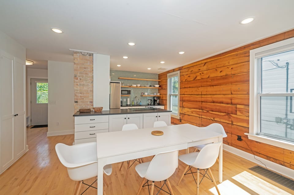 Dining for six against a warm wood accent wall, open to the kitchen.