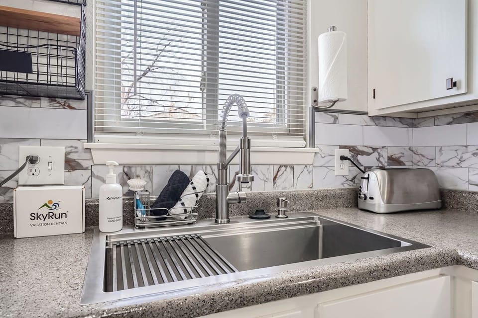 Your fully equipped kitchen features modern stainless steel fixtures and elegant marble backsplash, making meal prep a breeze while natural light streams through the window above the sink.