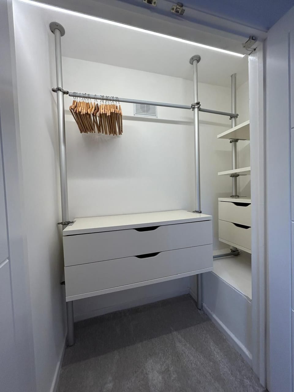 A spacious walk-in wardrobe featuring hanging rails with wooden hangers, two large drawers, open shelving, and a full-length mirror, providing ample storage to keep your clothes and belongings neatly organised during your stay.