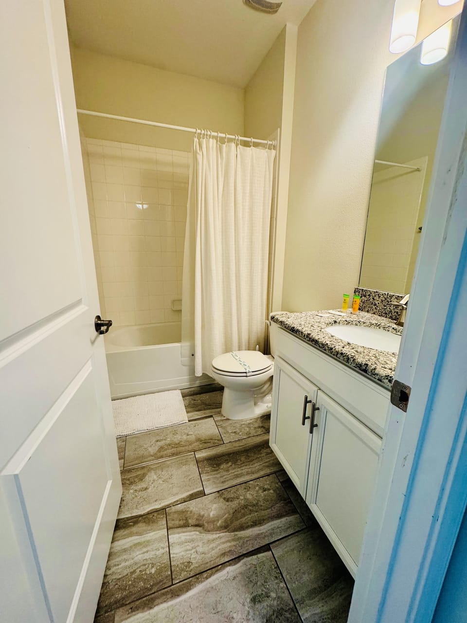 Bathroom with granite countertop, white cabinetry, tiled floors, and a bathtub with a cream shower curtain.