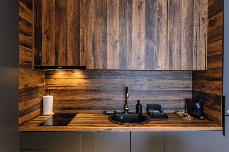 Kitchen worktop detail: round black sink, matte black tap and 2-ring induction hob set into a solid wood surface with rustic wood backsplash panelling. Premium kitchen finish in Grand Chalet Suite 2.