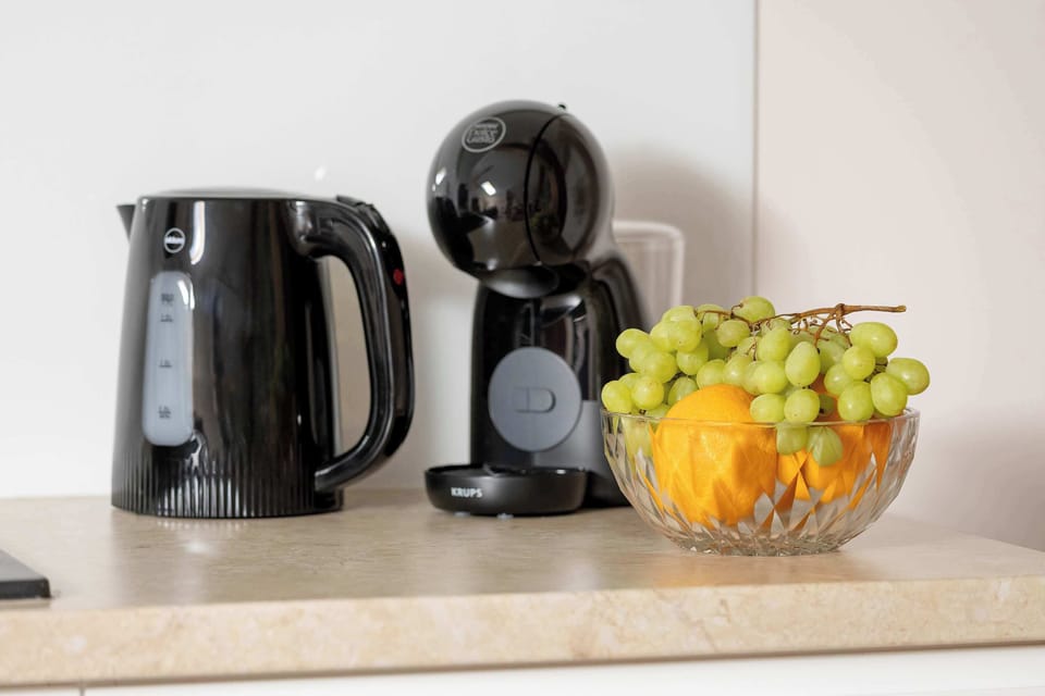 A kitchen countertop holds a black electric kettle, a coffee capsule machine. The setup provides a welcoming touch for incoming guests.