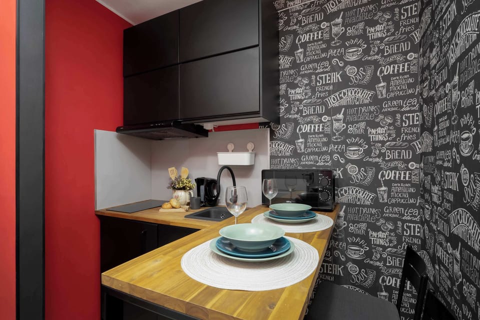 Modern kitchenette with wooden countertop, dark cabinets, dining area, and striking black-and-white patterned wall.