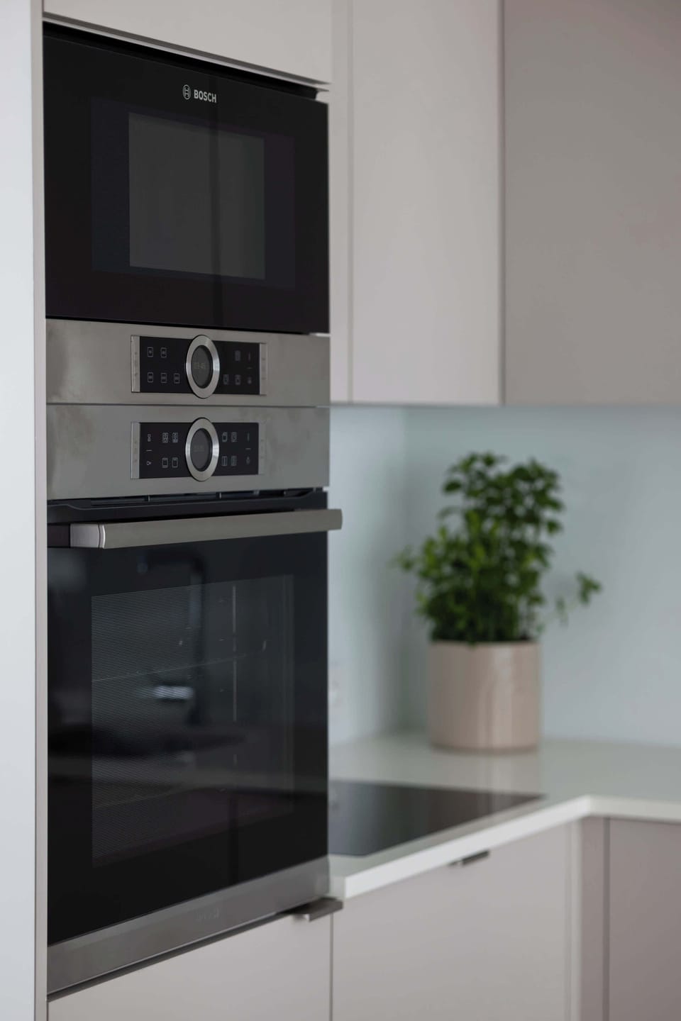 A detailed view of the kitchenette highlights a built-in oven and microwave stacked vertically. The modern appliances are seamlessly integrated into the light grey cabinetry for a clean look.