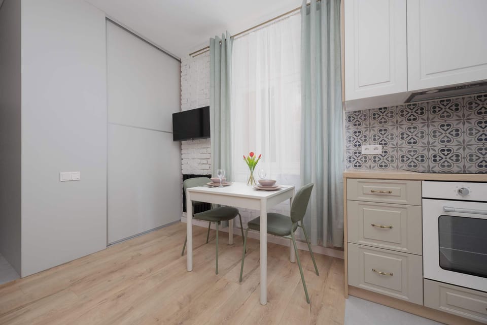 A white kitchenette is equipped with an oven and patterned backsplash. A dining table is placed next to the kitchen.