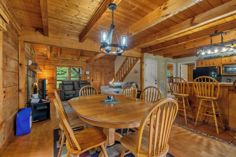 Round dining table under a wrought-iron chandelier, stairs climbing behind. Family-style dinners in a log-walled room — the meals everybody remembers from the trip.