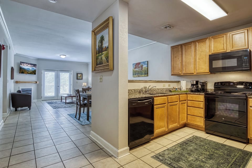 Wood cabinets, black appliances. rug.  tile floor. TV.  Living Room chairs. Door