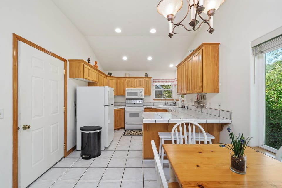 Cook up a feast in this bright, fully-equipped kitchen featuring warm wood cabinetry, white appliances, and a cozy dining spot bathed in natural light.