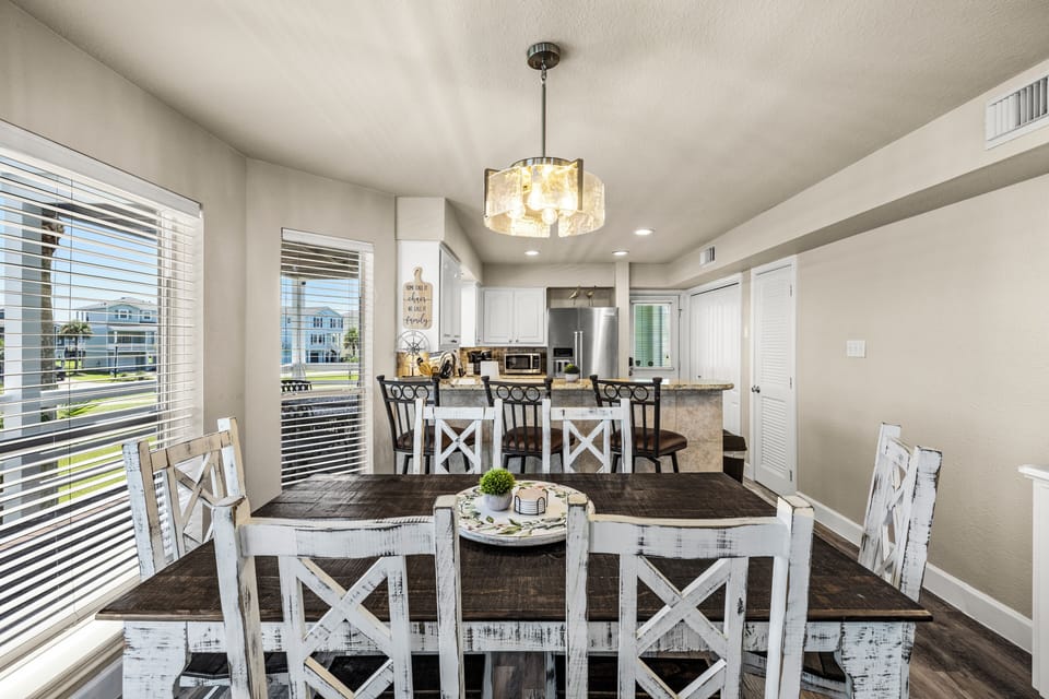 Spacious 6-seater dining area with seating for group meals, a statement chandelier, and additional bar-stool seating at the kitchen counter.