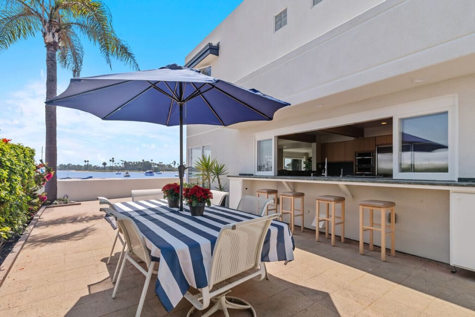 Expansive waterfront patio with outdoor dining, built-in BBQ bar, and panoramic bay views.