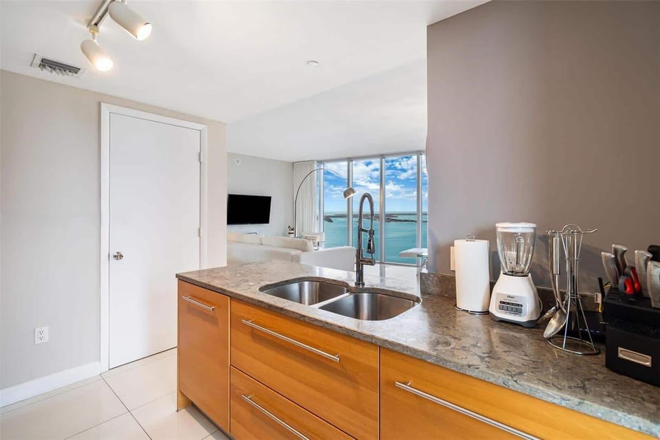 Fully equipped open kitchen with granite countertops, double sink, and stunning bay views right from the counter — cook with a waterfront backdrop.