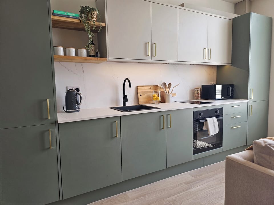 Sleek sage kitchen with gold accents, full appliances & warm lighting