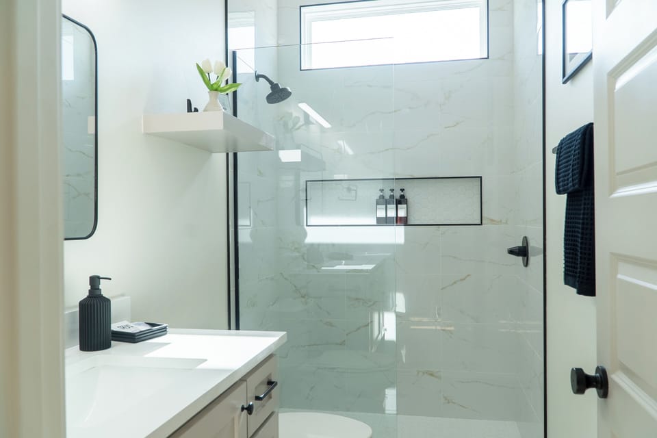 Enjoy a spa-like experience in the modern walk-in shower, featuring floor-to-ceiling tile, a frameless glass enclosure, and complimentary bath products.