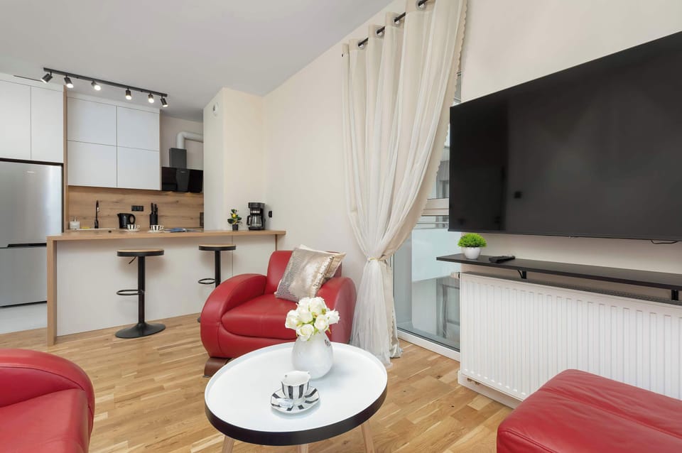 Bright living room featuring red leather sofas, a large TV, and an open-plan layout.