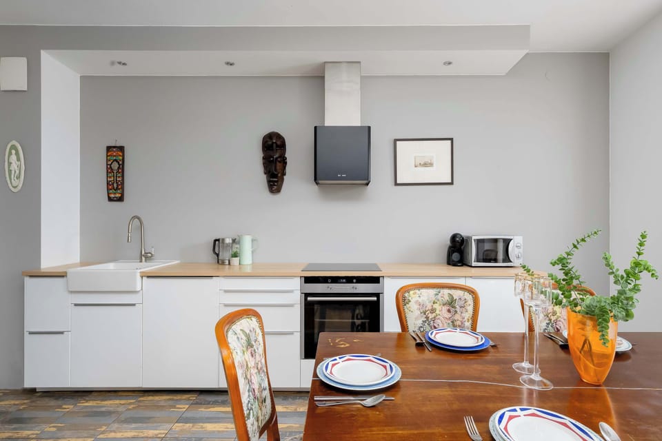 A modern kitchenette and dining space includes white cabinets and a light wooden countertop. A wooden dining table is partially visible, set with tableware for a meal.
