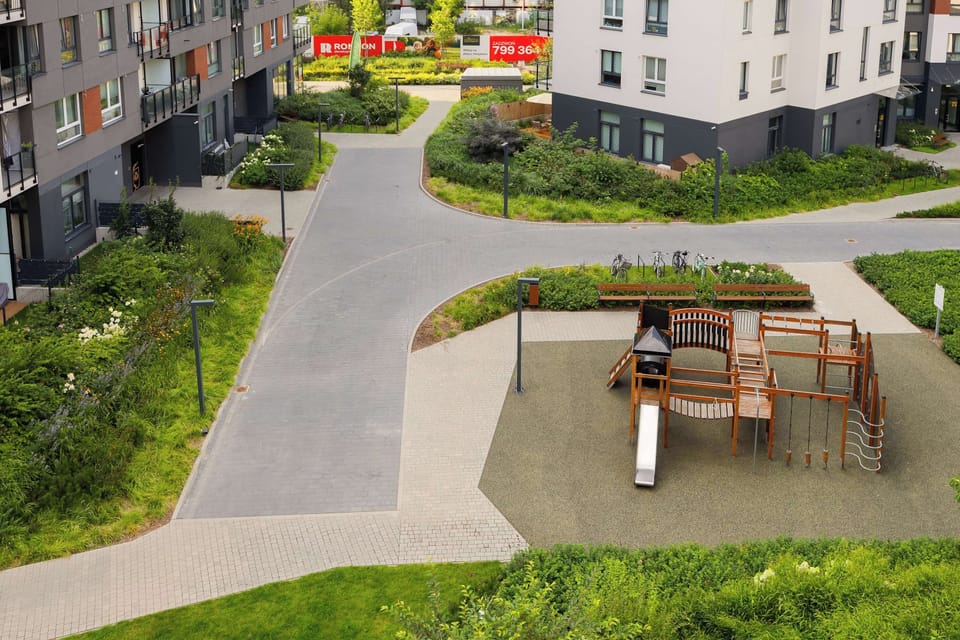 A high-angle perspective captures the outdoor communal garden area, featuring a small playground set on green lawns between residential blocks.