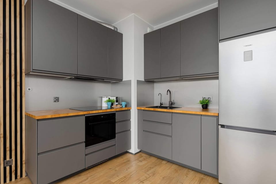 The kitchen corner features grey cabinetry paired with a built-in oven, black cooktop, and a freestanding silver refrigerator.