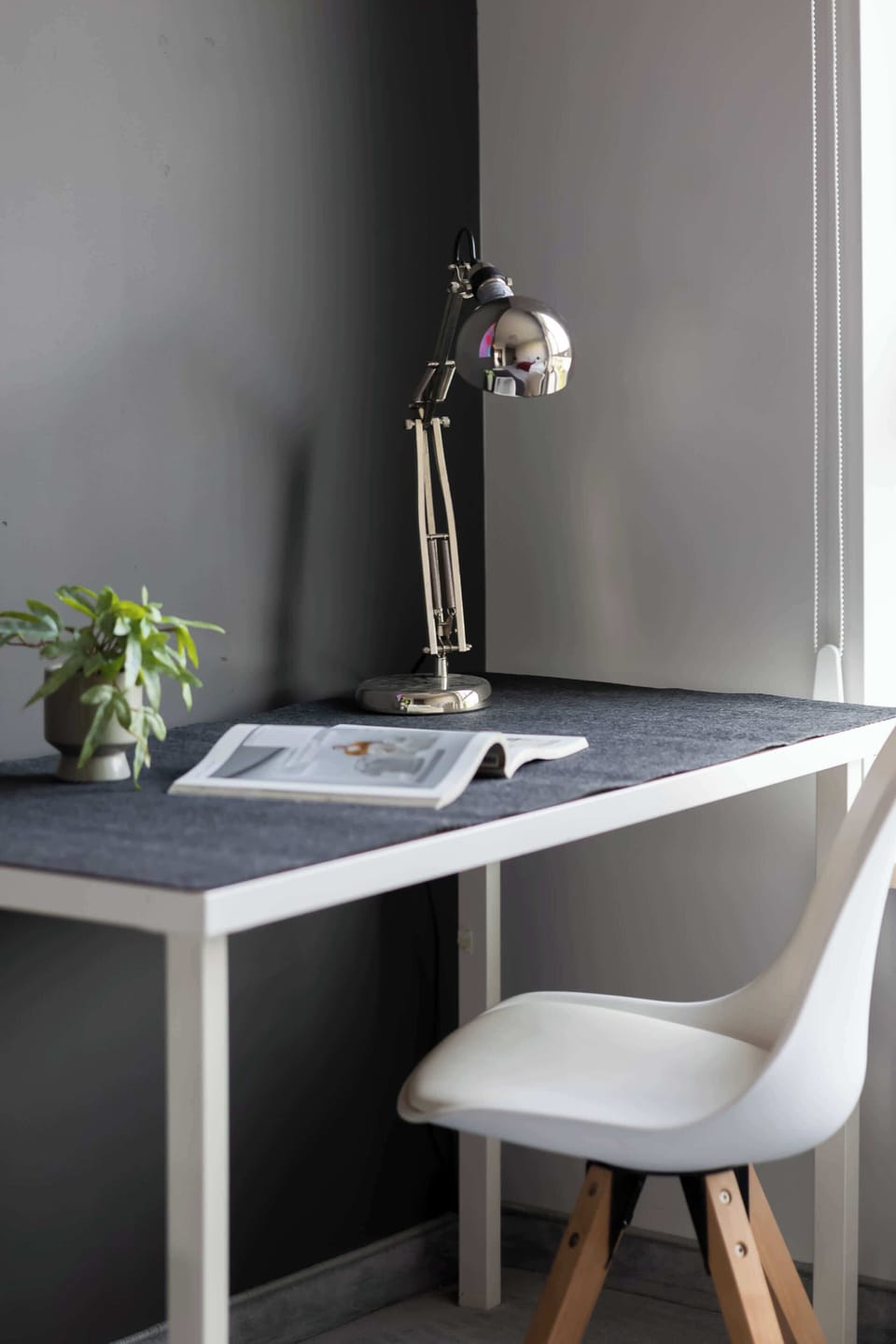 A detailed vertical close-up focuses on a small white study desk equipped with a metal desk lamp and a desk chair in the corner of the room.