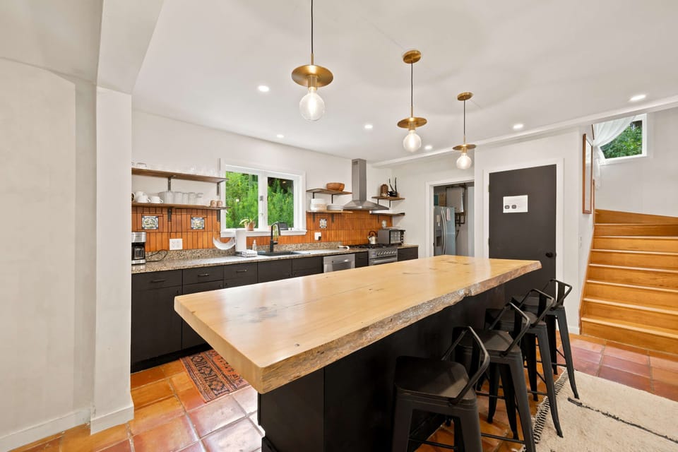 Gather around the wooden island with seating while you cook, with one of the home's two wooden staircases rising just beyond.