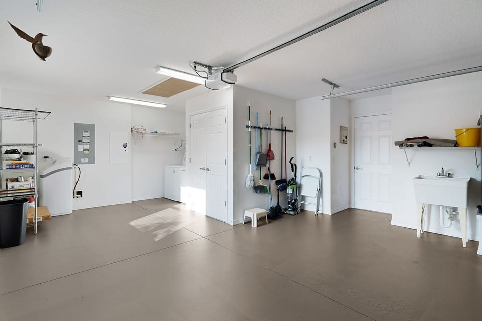 A pristine garage showcases thoughtful organization with wall-mounted tool racks, utility sink, and ample workspace. The well-lit space offers convenient access and practical storage solutions for your stay.