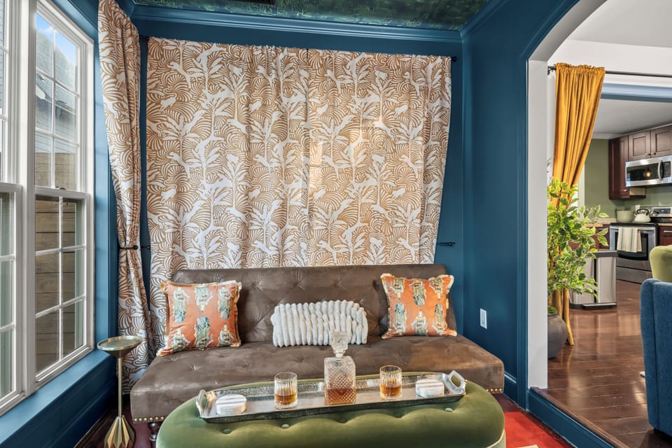 A moody blue nook with a tufted daybed, curtained backdrop, and a decanter tray on the velvet ottoman, the grown-ups' corner once the kids claim the cinema.