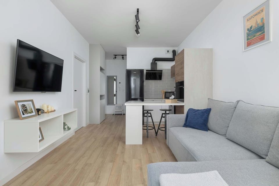 Spacious living room with a grey sectional sofa, TV, dining area, and open-plan kitchen.