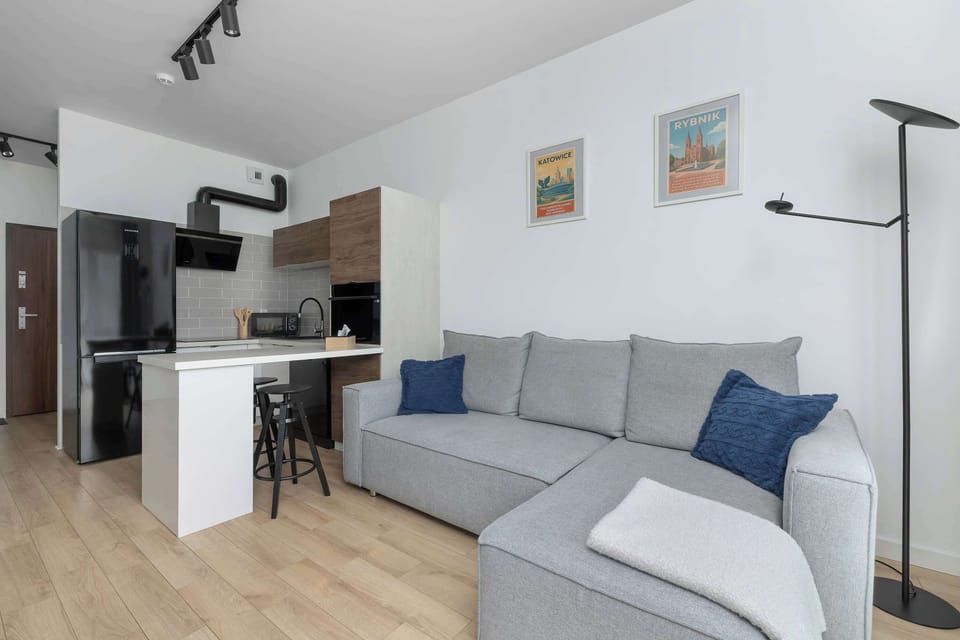 Bright living room with a comfortable grey sectional sofa, blue cushions, floor lamp, and large windows.
